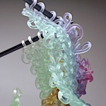 Loose knits flow from hands and needles in glass sculptures by Carol Milne
